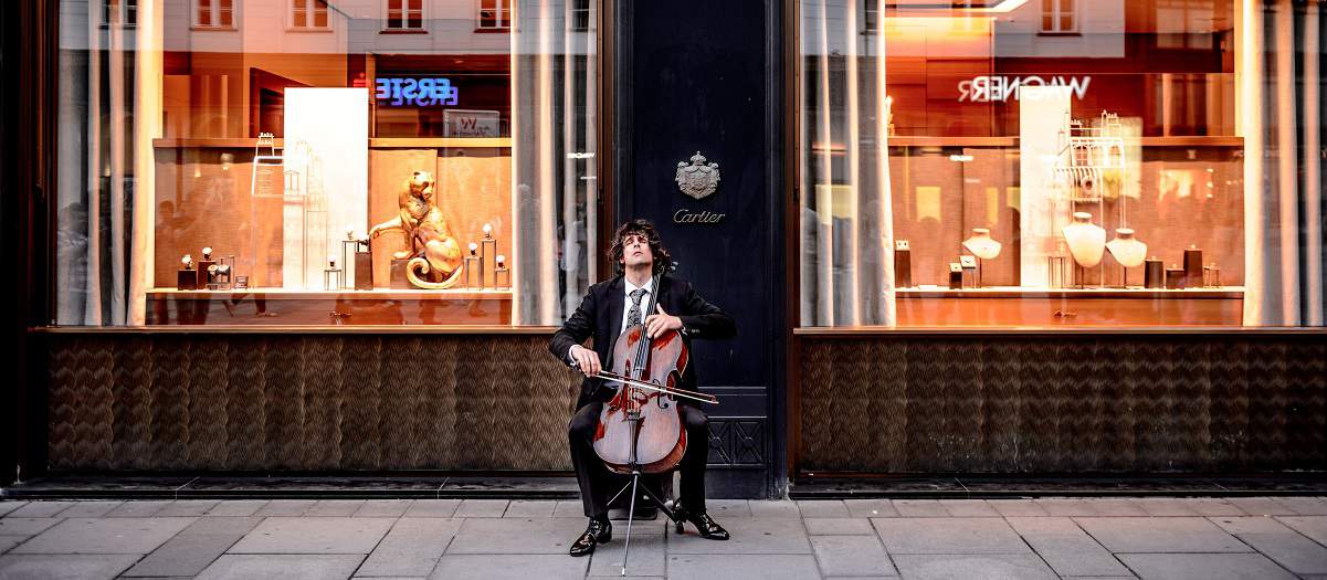 Person playing chello at front of a luxury retail store.